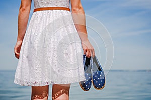 Woman holding moccasins on the beach walking in white dress photo