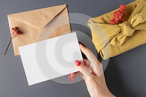 Woman holding mockup card over gray table with furoshiki gift