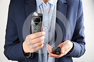 Woman holding modern breathalyzer and car key on light background, closeup