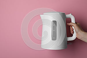 Woman holding modern electric kettle on pink background, closeup. Space for text