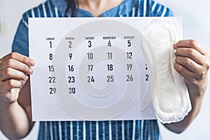 Woman holding monthly calendar and sanitary pads. Menstruation cycle calendar. Women health concept. Period days concept showing