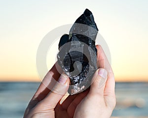 Woman holding Morion Smokey Quartz with Chlorite in her hand at sunrise