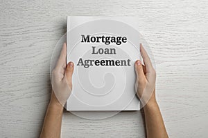 Woman holding mortgage loan agreement on white wooden table, top view