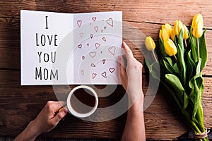 Woman holding Mothers day greeting and coffee. Yellow tulips.