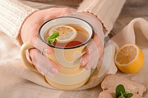 Woman holding mug of hot lemon tea with ginger at table