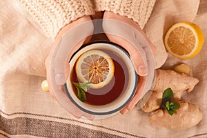 Woman holding mug of hot lemon tea with ginger, top view