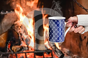 Young woman relaxing in front of cozy fireplace and warming up her feet in woolen socks in country house.