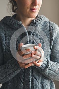 Woman holding mug of tea wearing cozy gray cardigan