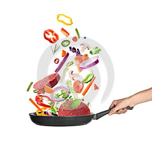 Woman holding nonstick frying pan with falling beef slices and vegetables on background. Process of cooking