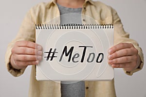 Woman holding notebook with hashtag MeToo against light background. Stop sexual assault