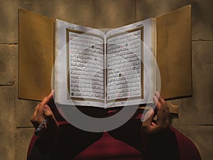 A woman holding an open Quran on a wooden stand