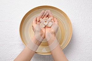 Woman holding orchid flower above bowl with water on white towel, top view