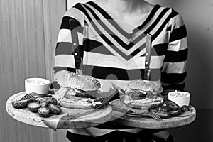 Woman holding pair of round wooden trays with burgers