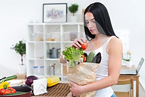 Woman holding paper bag with fresh grocery looking down attentively, choosing ingredients for diet healthy meal.