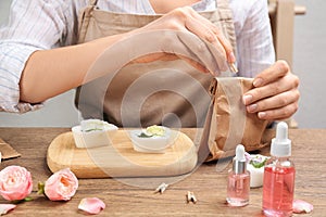 Woman holding paper bag with handmade soap at wooden table, closeup