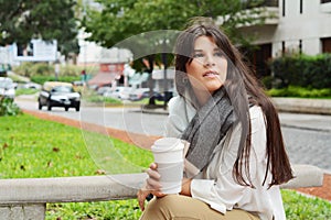 Woman holding paper coffee cup in the street.
