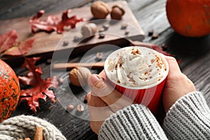 Woman holding paper cup with tasty pumpkin spice latte at black wooden table