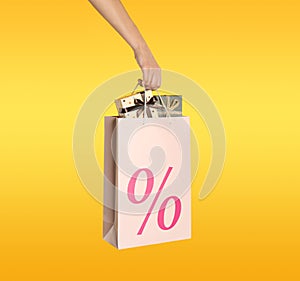 Woman holding paper shopping bag with percent sign on yellow background, closeup. Discount concept