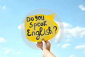 Woman holding paper speech bubble with question Do You Speak English against blue sky, closeup