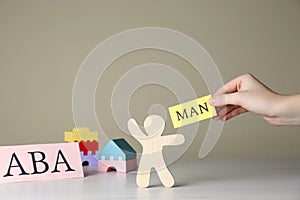Woman holding paper with word Man near human figure and abbreviation ABA Applied behavior analysis at white wooden table,