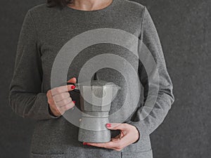 Woman holding percolator in gray clothing over a gray backgroud