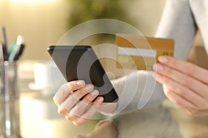 Woman holding phone and credit card on a desk at home