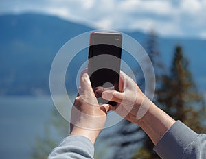 A woman holding phone showing Black screen. Women's hands holding cell telephone taking photos or videos of the nature