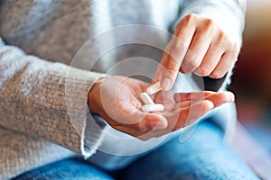 A woman holding and picking white medicine capsules in hand