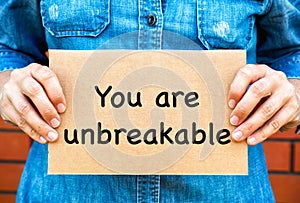 Woman holding a piece of a cardboard with words You Are Unbreakable