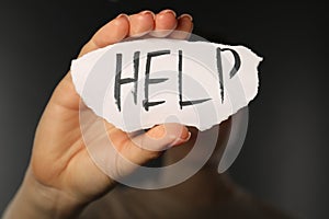 Woman holding piece of paper with word Help on black background, closeup. Domestic violence concept