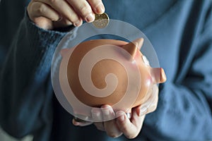 Woman holding piggy bank and putting coin in it