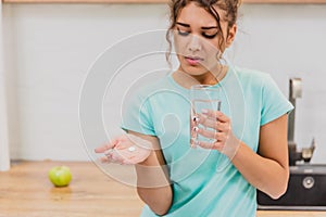 Woman holding pill and glass of water in hands taking emergency medicine, supplements or antibiotic antidepressant