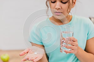 Woman holding pill and glass of water in hands taking emergency medicine, supplements or antibiotic antidepressant