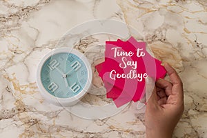 Woman holding a pink card with time to say goodbye text with alarm clock