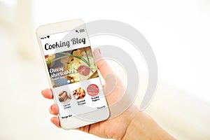 Woman holding a pink gold blank smartphone showing cooking blog