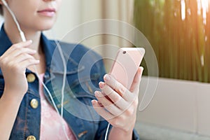 Woman holding pink phone and listening to music on headphones