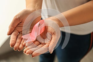 Woman holding pink ribbon, closeup. Breast cancer awareness concept