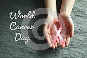Woman holding pink ribbon on stone background, top view. World Cancer Day