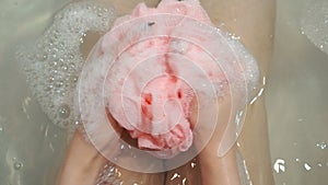 Woman holding pink sponge and soaping it using shower gel.