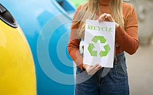 Woman Holding Placard With Green Recycle Sign Standing Near Colorful Garbage Containers