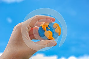 Woman holding planet Earth in her hand against blue sky