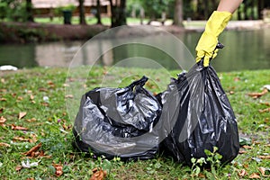 Woman holding plastic bags with garbage in park, closeup