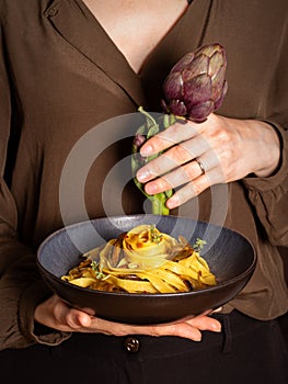 Woman holding a plate with artichokes pasta, fettucine, seasoned with saffron