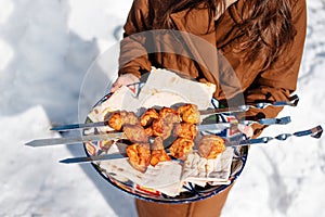 Woman holding plate with meat against the background of winter snow