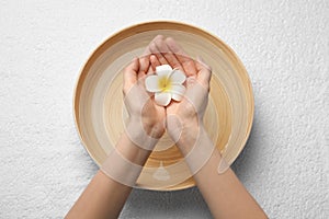 Woman holding plumeria flower above bowl with water on white towel, top view