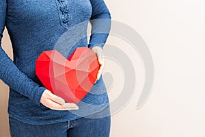 Woman holding polygonal diamond shaped red heart in front of her body