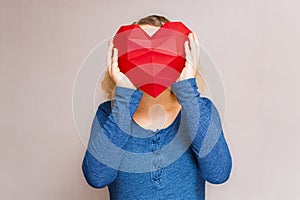 Woman holding polygonal diamond shaped red heart in front of her face