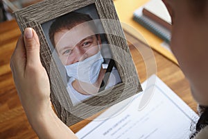 Woman holding portrait of deceased husband with improperly wearing protective medical mask closeup