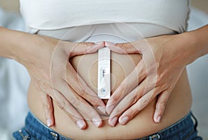 Woman holding positive pregnancy test with heart shape