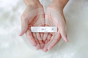 Woman holding positive pregnancy test in her palm on artificial white fur background